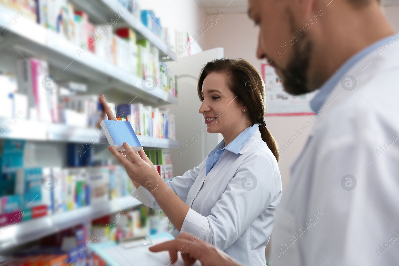 Photo of Professional pharmacists near shelves with merchandise in modern drugstore