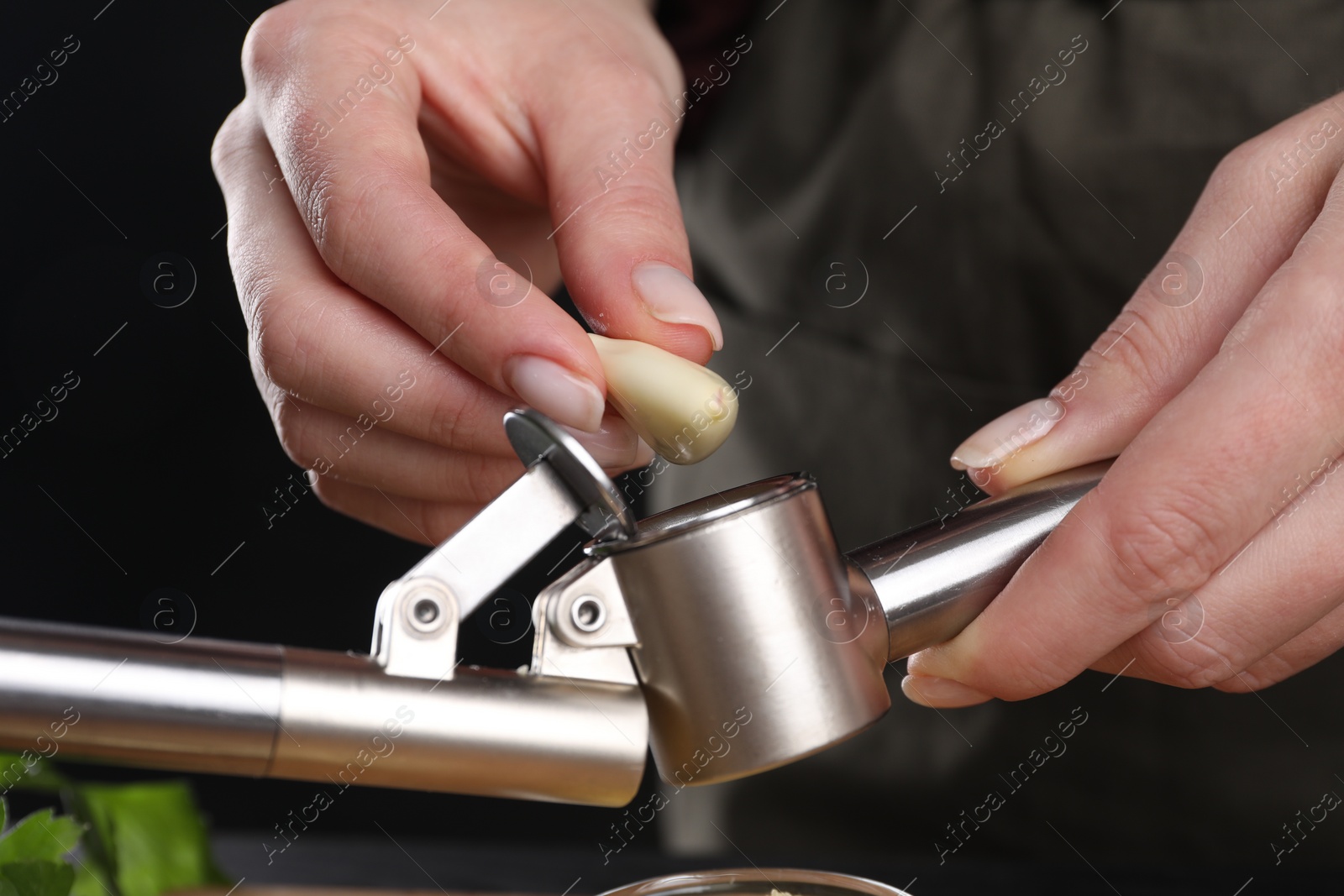 Photo of Woman putting garlic clove into press on blurred background, closeup