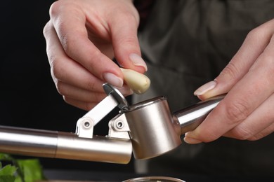 Photo of Woman putting garlic clove into press on blurred background, closeup