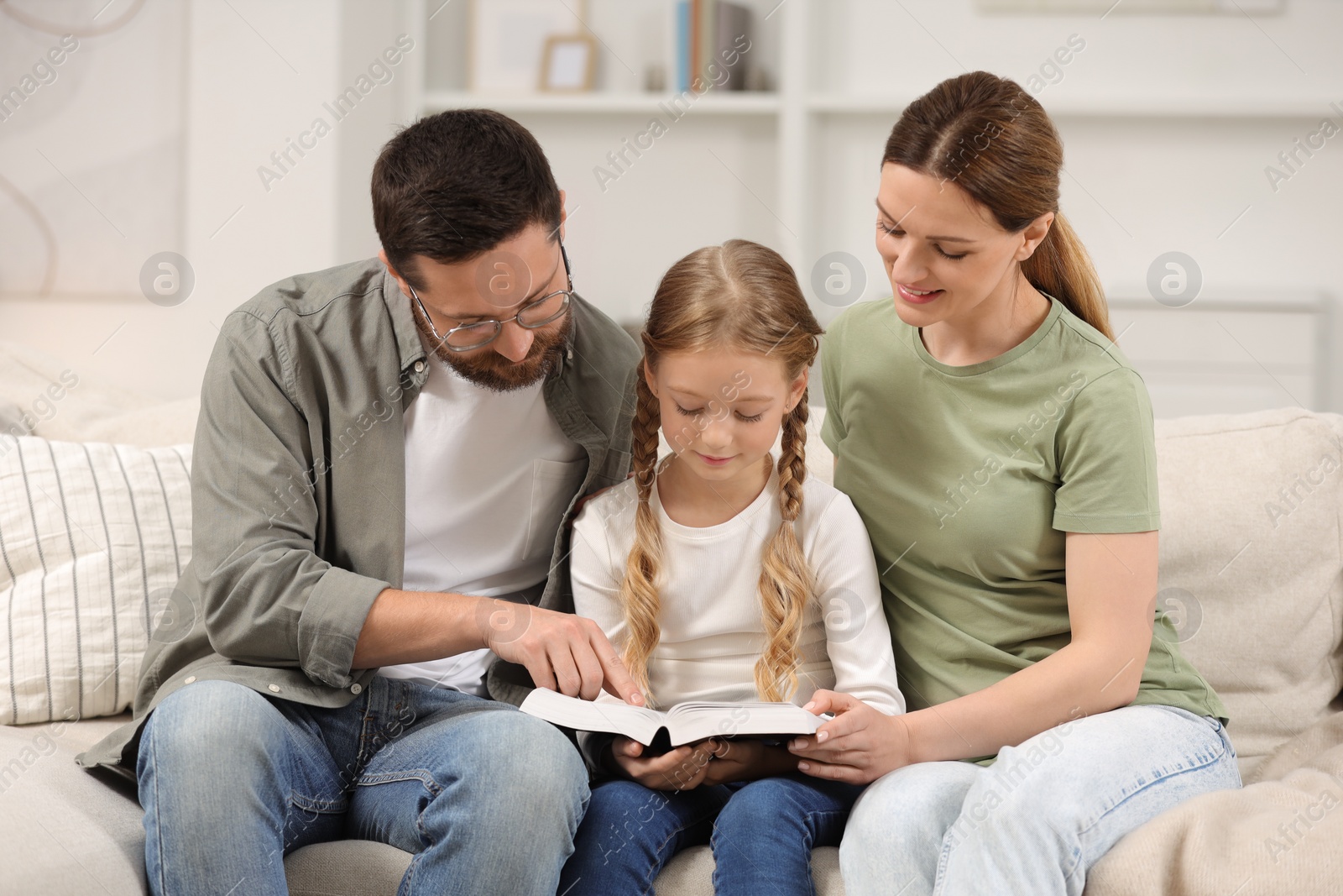 Photo of Girl and her godparents reading Bible together on sofa at home