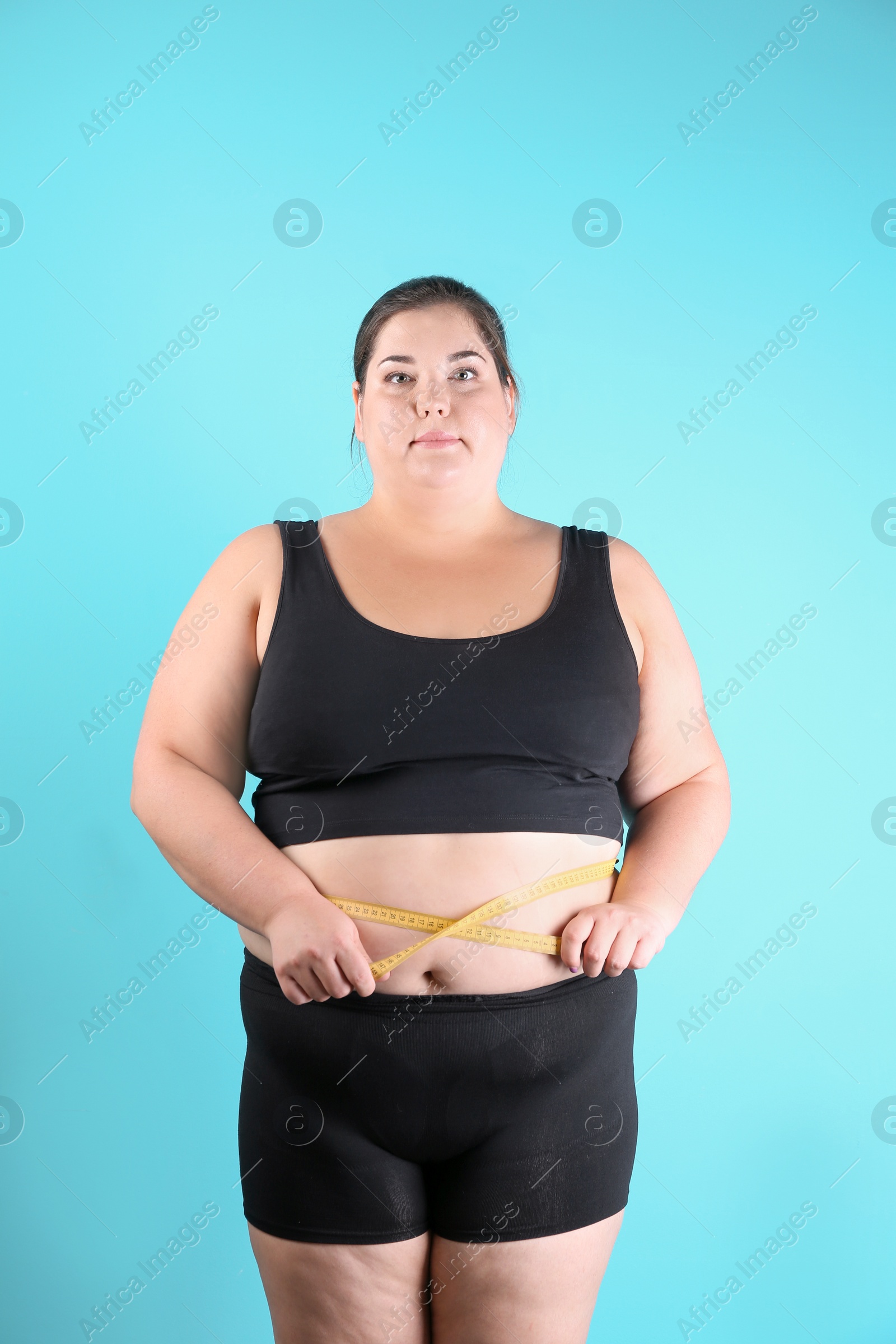 Photo of Overweight woman measuring waist before weight loss on color background