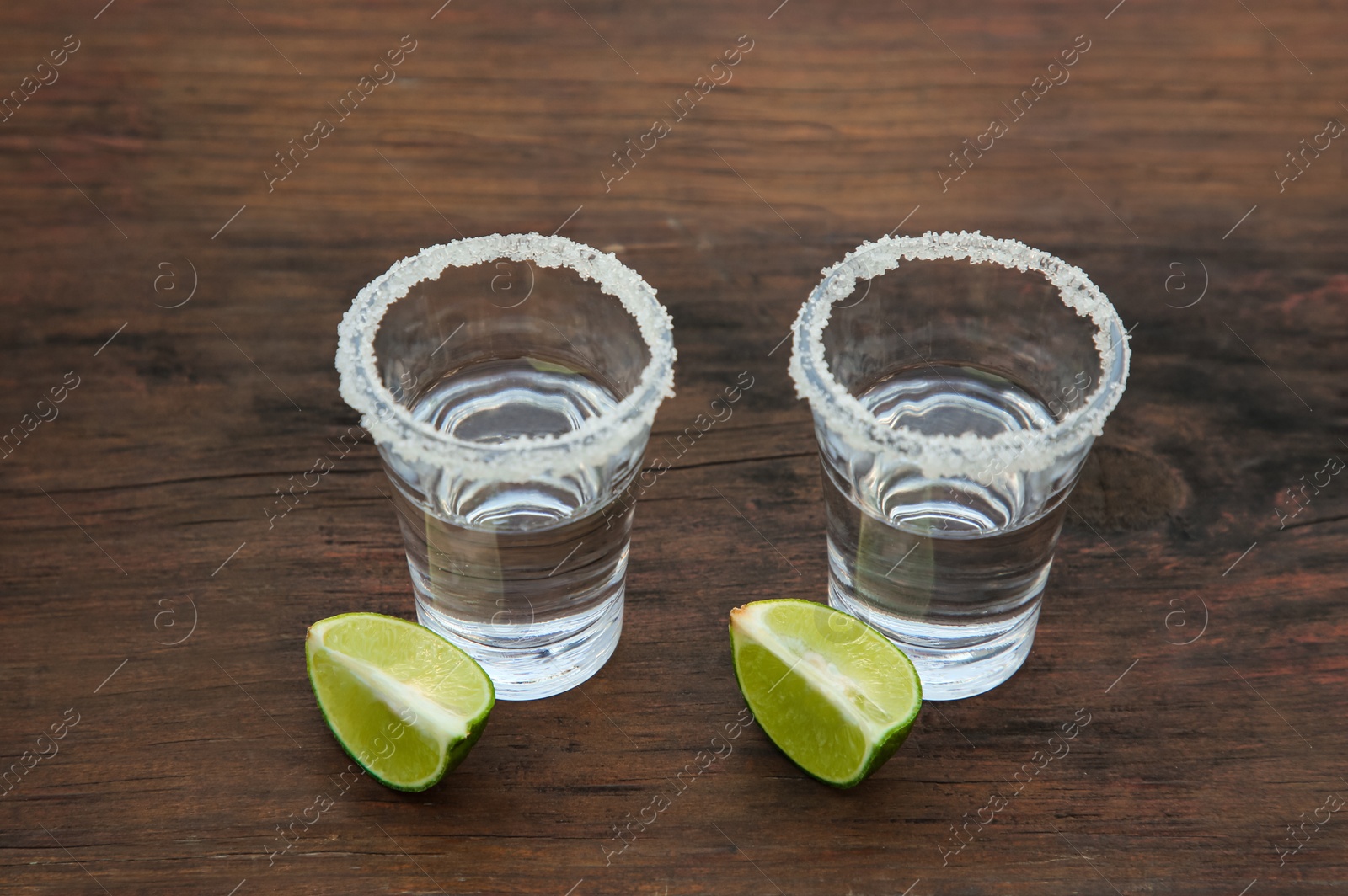 Photo of Mexican tequila shots with lime slices and salt on wooden table