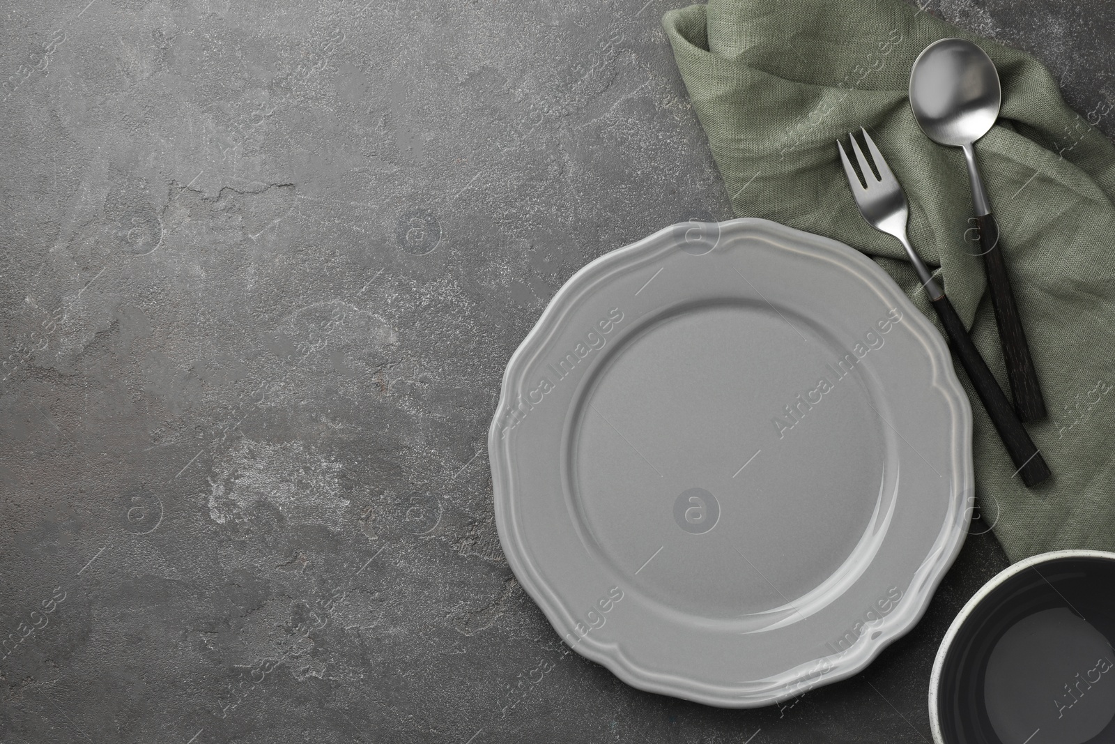 Photo of Stylish setting with cutlery, napkin and plate on grey textured table, top view. Space for text