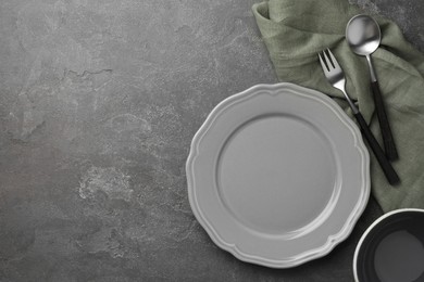 Stylish setting with cutlery, napkin and plate on grey textured table, top view. Space for text