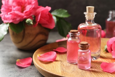 Photo of Wooden tray with bottles of rose essential oil and petals on table, space for text