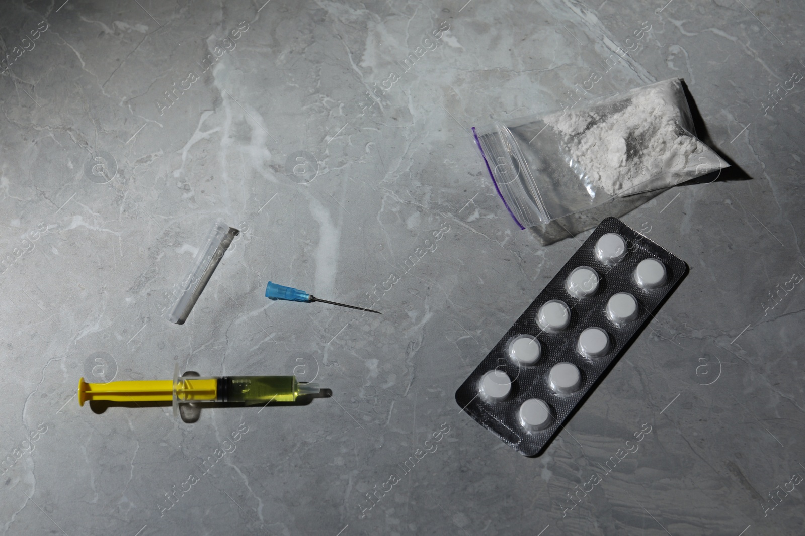 Photo of Pills, syringe and powder on grey marble table, above view. Hard drugs