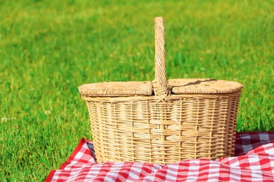 Picnic basket with checkered tablecloth on green grass outdoors, space for text