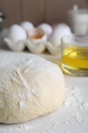 Photo of Fresh yeast dough with flour on white wooden table, closeup