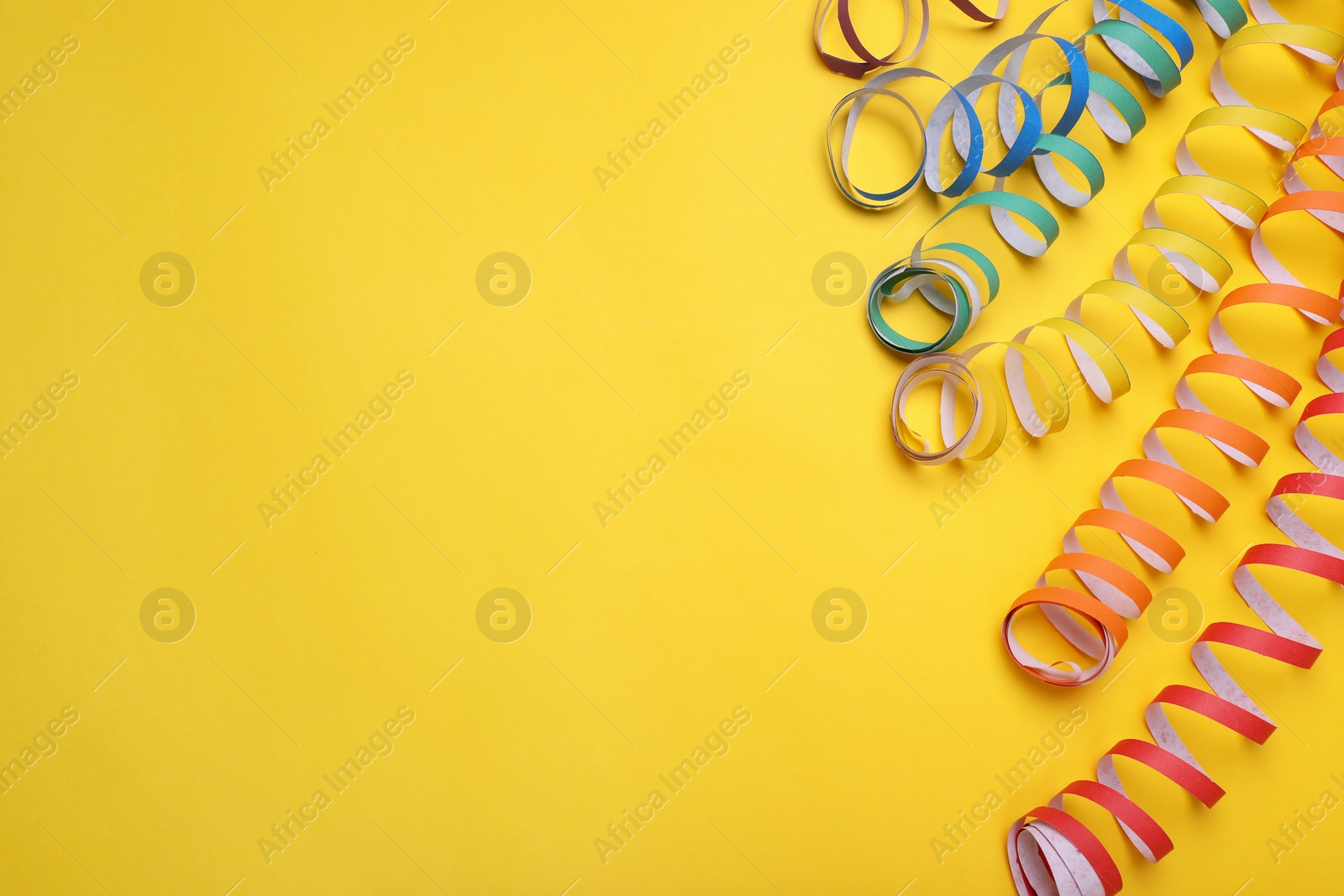 Photo of Rainbow serpentine streamers on yellow background, flat lay with space for text. LGBT pride