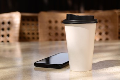 Photo of Takeaway coffee cup and smartphone on beige table in cafe