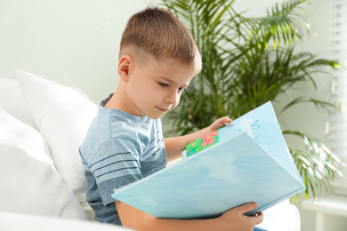 Photo of Little boy reading book on sofa indoors