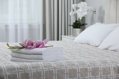 Photo of Stack of clean towels and gladiolus flowers on bed indoors, space for text