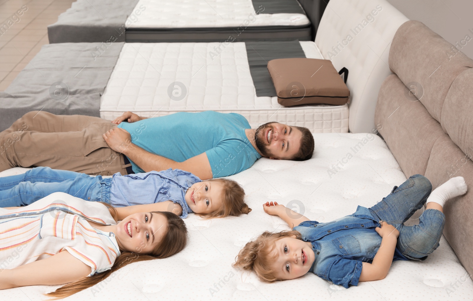 Photo of Happy family lying on new orthopedic mattress in store