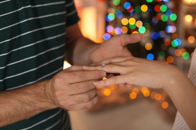 Photo of Man putting wedding ring on his girlfriend's finger at home. Christmas surprise