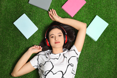 Young woman listening to audiobook while lying on grass, flat lay