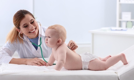 Photo of Children's doctor examining baby with stethoscope in hospital. Space for text