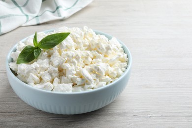 Photo of Fresh cottage cheese with basil in bowl on light wooden table