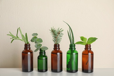 Glass bottles of different essential oils with plants on table