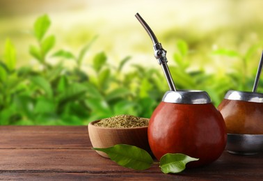 Calabashes with mate tea and bombilla on wooden table outdoors. Space for text