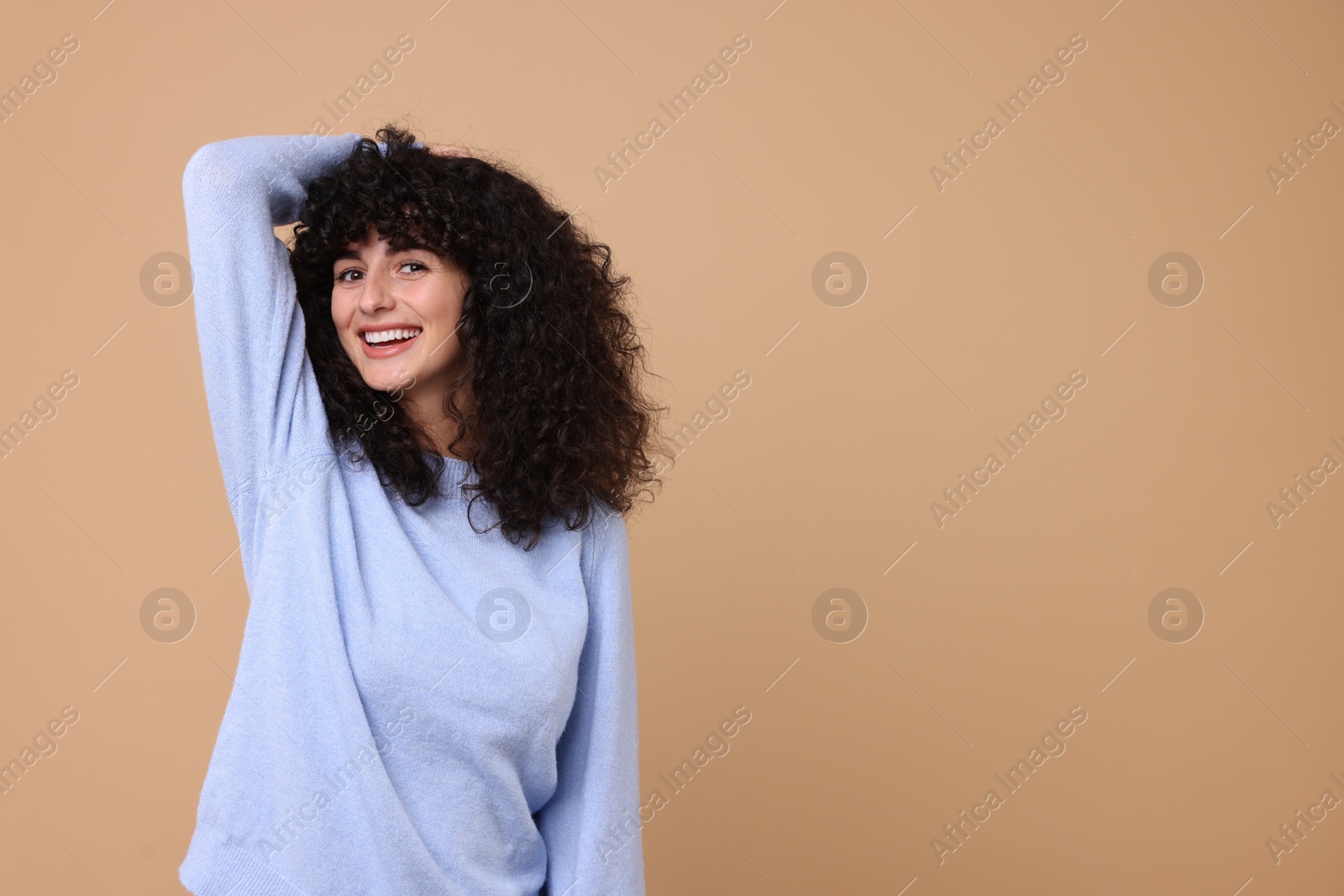 Photo of Happy young woman in stylish light blue sweater on beige background, space for text