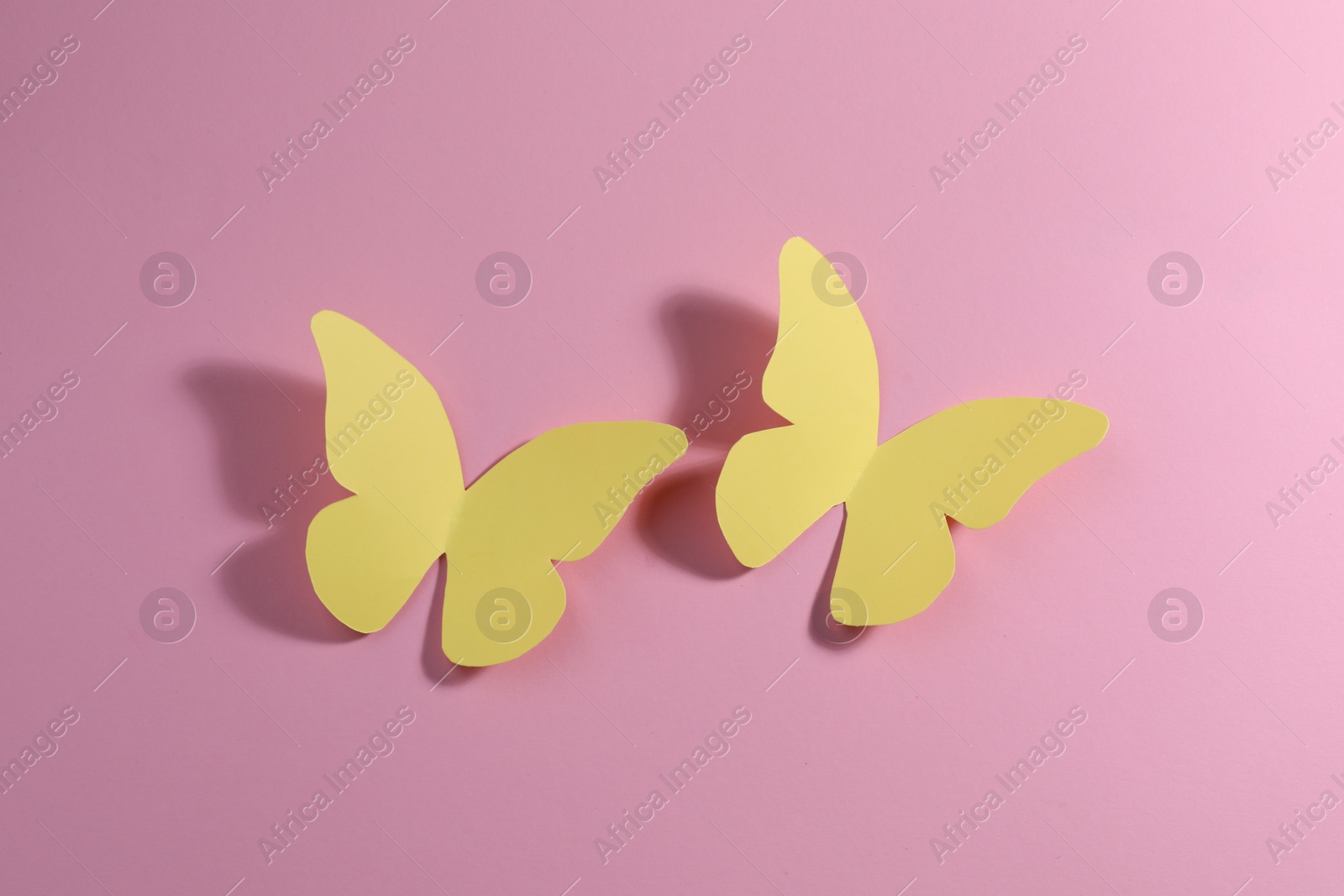 Photo of Yellow paper butterflies on pink background, top view