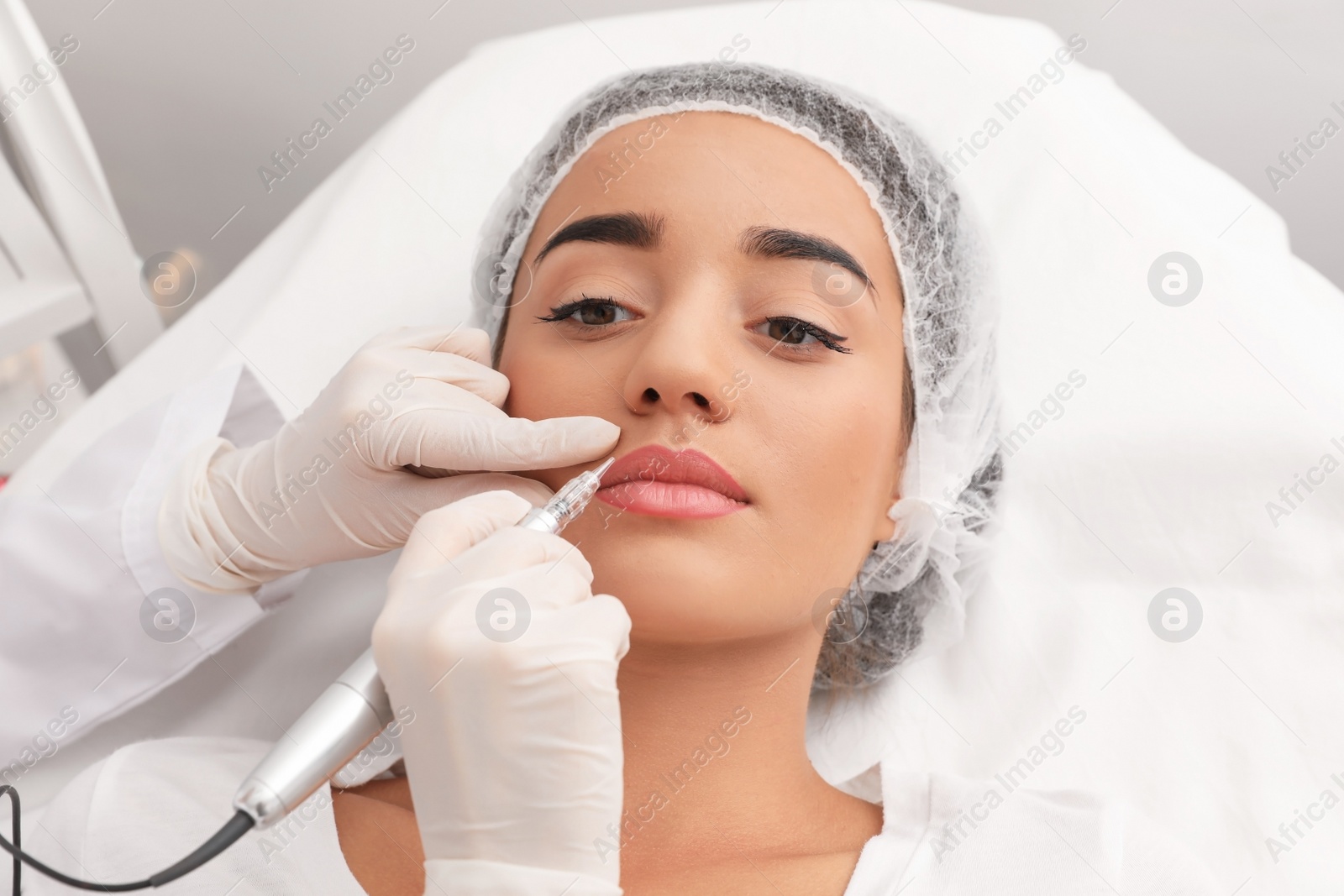 Photo of Young woman undergoing procedure of permanent lip makeup in tattoo salon