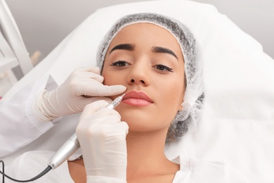 Photo of Young woman undergoing procedure of permanent lip makeup in tattoo salon