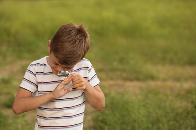 Photo of Cute little boy exploring ladybug outdoors, focus on magnifying glass. Child spending time in nature