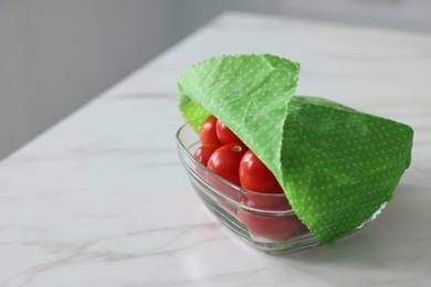 Tomatoes in bowl covered with beeswax food wrap on white table, closeup. Space for text