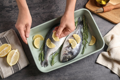 Woman adding lemon to raw dorada fish on grey table, top view