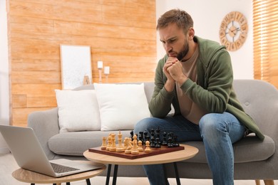 Photo of Thoughtful young man playing chess with partner through online video chat in living room