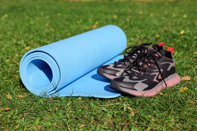 Photo of Bright karemat or fitness mat and sportive shoes on fresh green grass outdoors