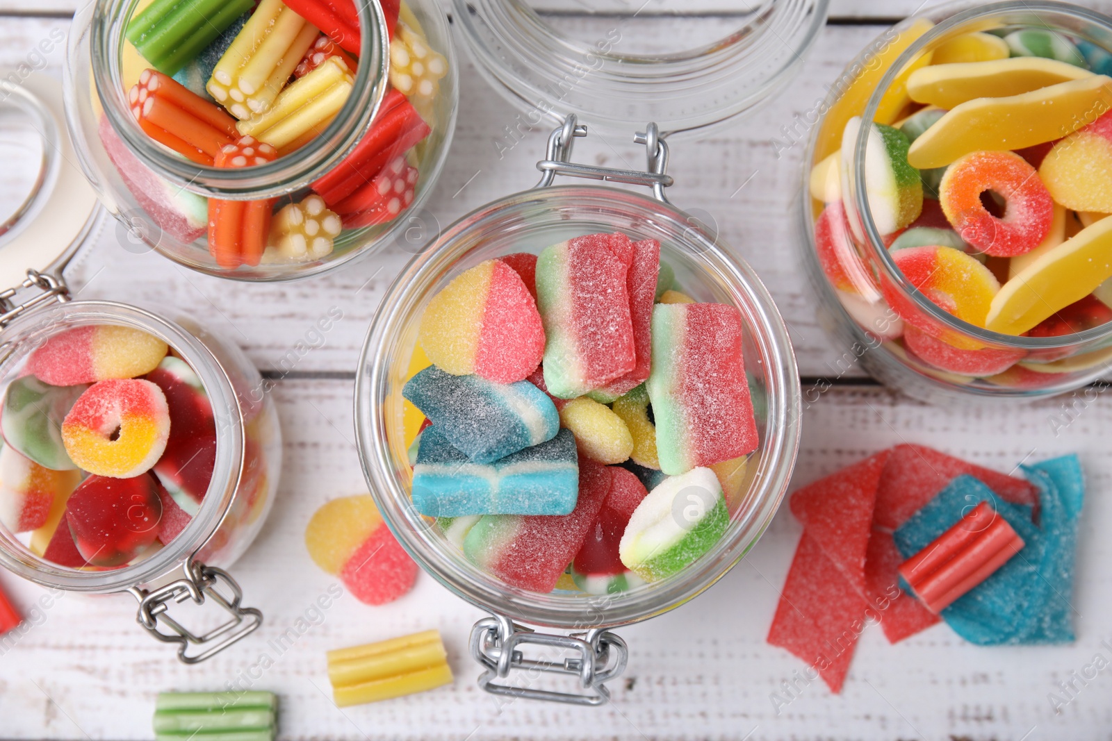 Photo of Tasty jelly candies in different jars on white wooden table, flat lay