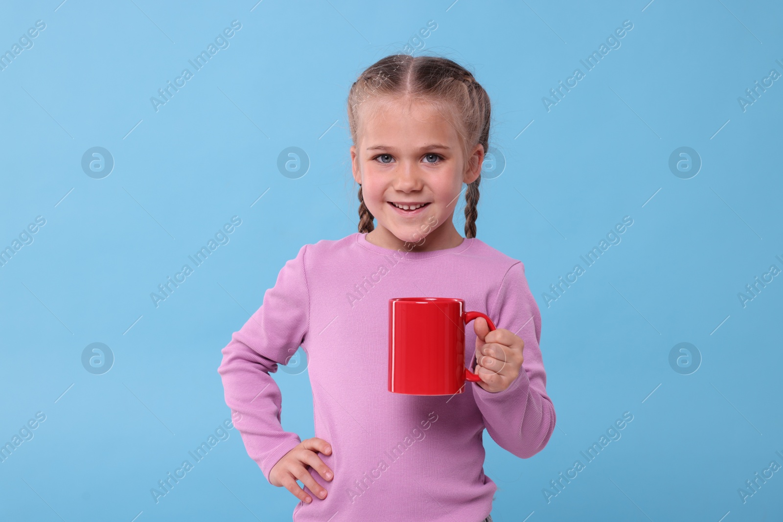 Photo of Happy girl with red ceramic mug on light blue background