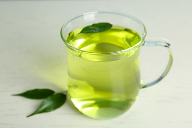 Photo of Cup of aromatic green tea and leaves on light wooden table