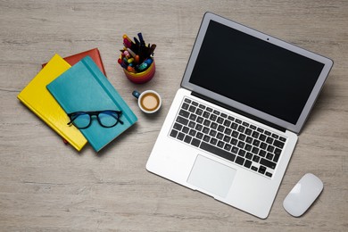 Modern laptop, cup of coffee and office stationery on white wooden table, flat lay. Distance learning