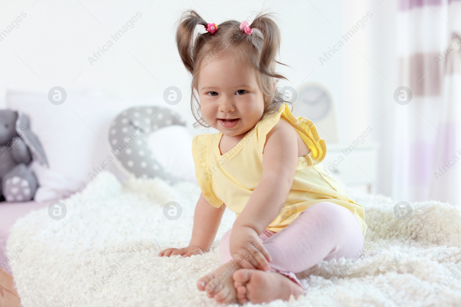 Photo of Adorable little baby girl sitting on bed in room