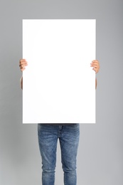 Man holding white blank poster on grey background. Mockup for design