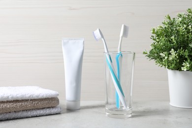 Photo of Plastic toothbrushes in glass holder, tube of toothpaste and towels on light grey table