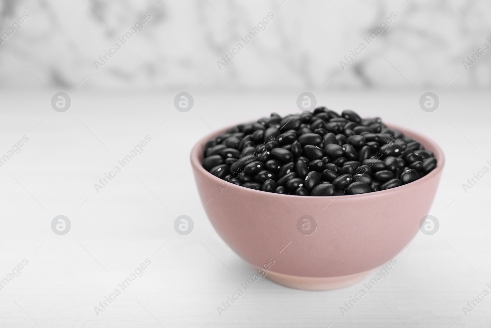 Photo of Bowl of raw black beans on white wooden table. Space for text
