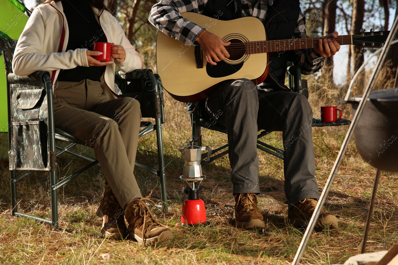 Photo of Couple with guitar resting in camping chairs outdoors, closeup