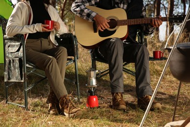 Couple with guitar resting in camping chairs outdoors, closeup