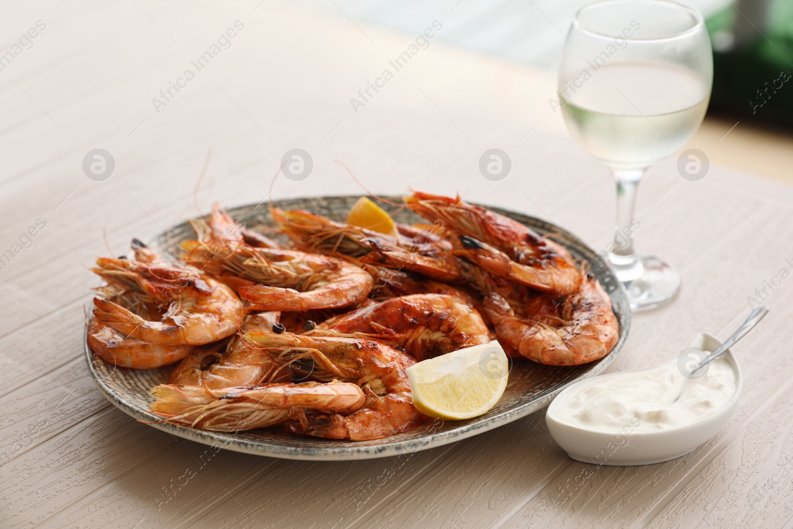 Photo of Plate of delicious cooked shrimps served with lemon, sauce and wine at table