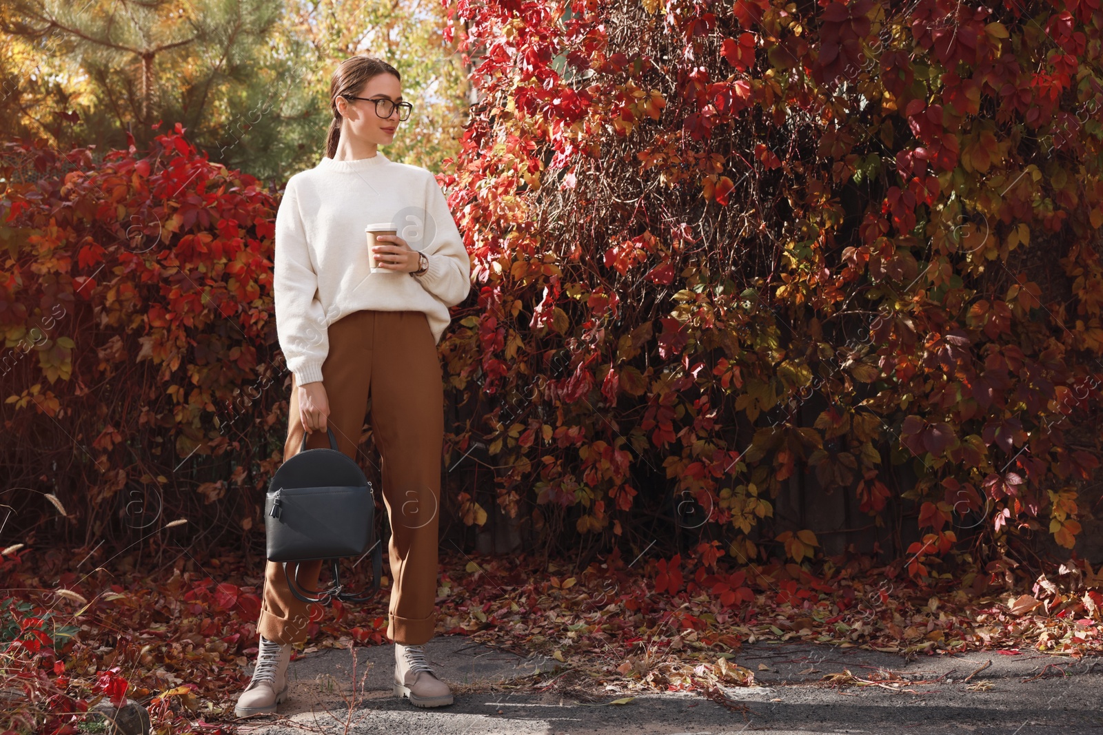 Photo of Beautiful young woman with stylish grey backpack and hot drink in autumn park