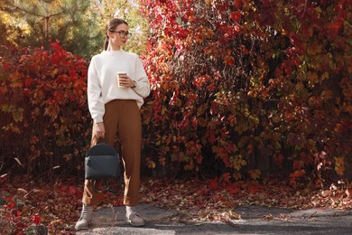 Beautiful young woman with stylish grey backpack and hot drink in autumn park