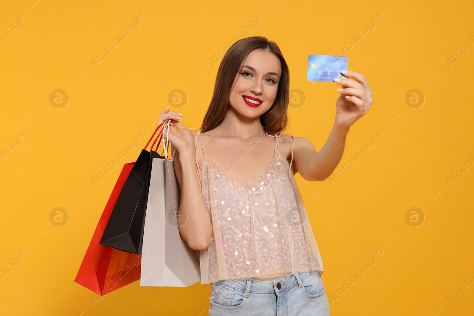 Photo of Stylish young woman with shopping bags and credit card on orange background