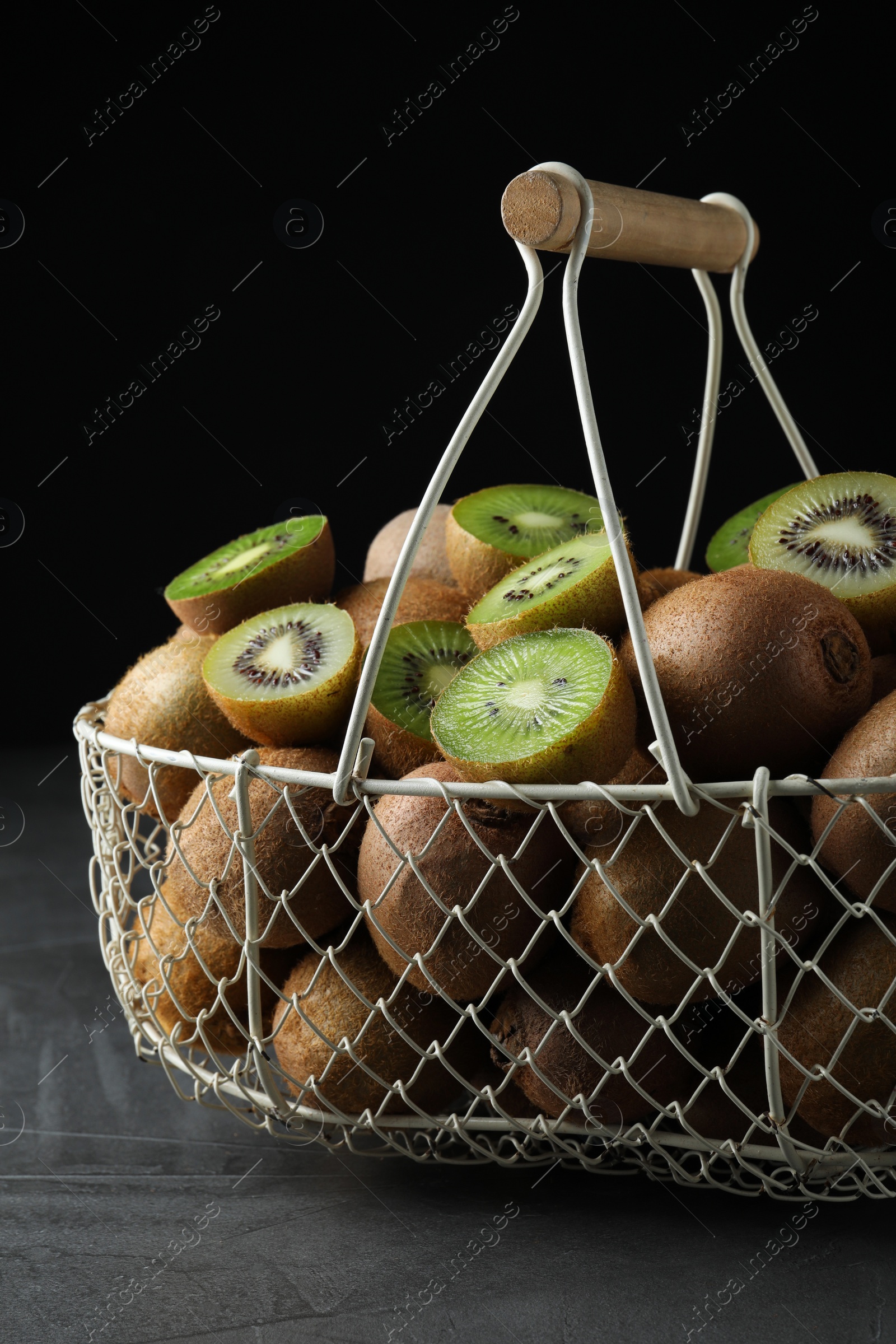 Photo of Fresh ripe kiwis in metal basket on grey table against dark background