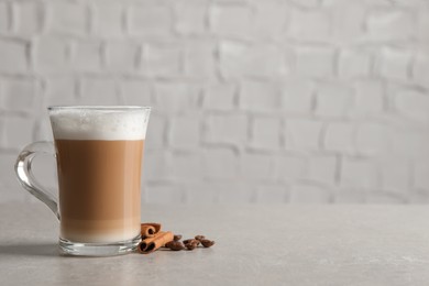 Glass cup of delicious layered coffee, beans and cinnamon on light grey table near white wall, space for text