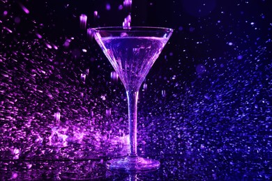 Photo of Glass of martini and splashes in neon lights on dark blue background, bokeh effect