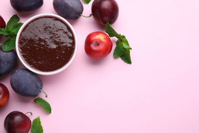 Plum puree in bowl and fresh fruits on pink background, flat lay. Space for text